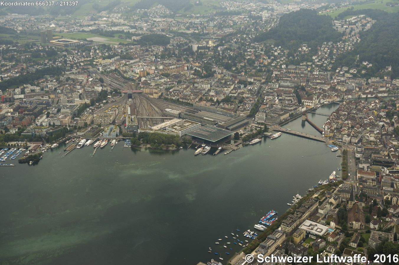 Luzern mit Hauptbahnhof, KKL (Postition 2'666'369.58, 1'211'414.54) und Kapellbrücke, Blickrichtung SSW (Horw). - Wasserturm (am Ende der Kapellbrücke), westwärts Jesuitenkirche, weiter am oberen rechten Bildrand: Siedlung in der Waldlichtung Untergütsch und Obergütsch. Stadion rechte obere Bildecke: Swisspor Arena. - Untere Bildecke: Hofkirche und 'Nationalquai'.